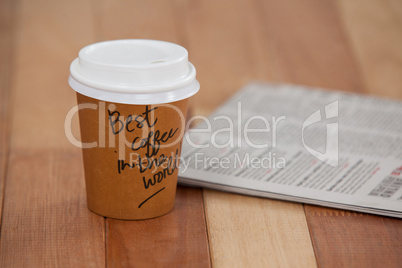 Close-up of disposable coffee cup and newspaper