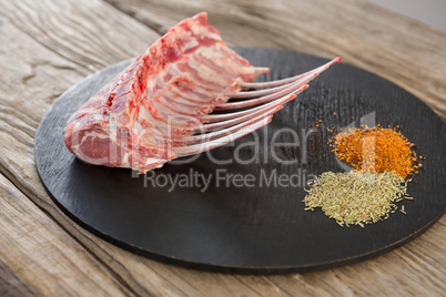 Beef ribs rack and spices on black round tray against wooden background