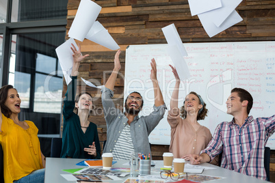 Team of excited graphic designers throwing document in the air during meeting