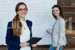 Portrait of businesswoman using digital tablet while colleague working in background