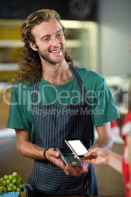 Smiling male staff receiving a payment through nfc technology at counter