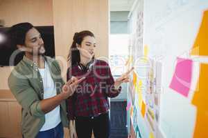 Male and female graphic designers discussing over sticky notes