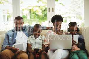 Parents and kids using laptop, smartphone and digital tablet on sofa