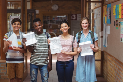 Portrait of happy classmates holding grade cards in corridor