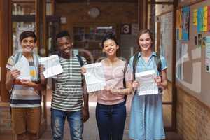 Portrait of happy classmates holding grade cards in corridor