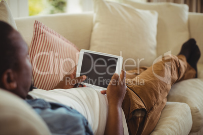 Man lying on sofa and using digital tablet