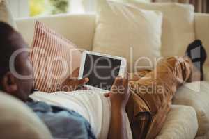 Man lying on sofa and using digital tablet