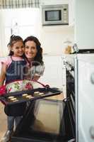 Mother and daughter holding tray of baked cookies in kitchen