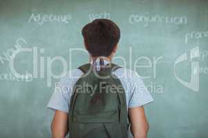 Rear view of schoolboy with backpack reading chalkboard in classroom