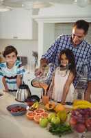 Father preparing smoothie with his kids in kitchen