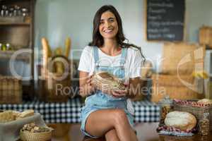 Portrait of smiling woman sitting at counter holding a round loaf of bread