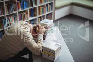 Tensed school teacher leaning on table in library