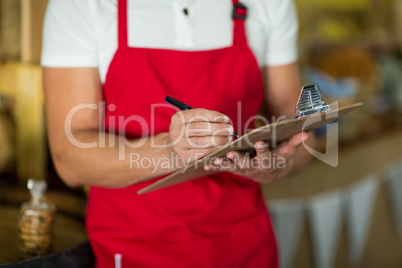 Mid section of bakery staff writing on clipboard at counter