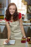 Female shop assistant writing on the clipboard at the counter