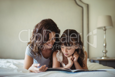 Mother and daughter reading a book while lying on bed