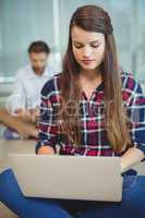 Female executive sitting on floor and using laptop