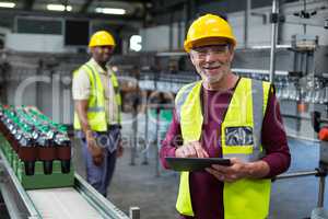 Smiling factory worker with digital tablet standing near the production line