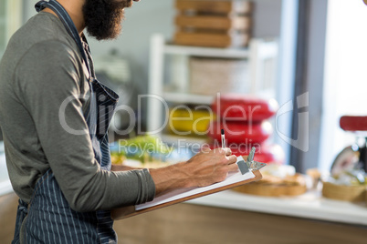 Mid section of salesman writing on clipboard at counter