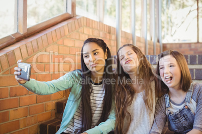 Smiling schoolgirls sitting on the staircase taking selfie with mobile phone