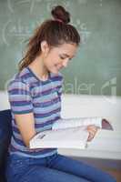 Schoolgirl sitting on chair and holding a book in classroom