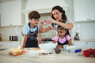 Mother and kids breaking egg in the bowl while preparing cookie