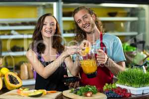 Smiling shop assistant preparing juice at health grocery shop