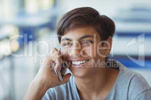 Happy schoolboy talking on mobile phone in classroom