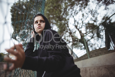 Anxious teenage girl leaning on wire mesh fence