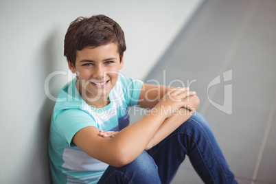 Portrait of happy schoolboy sitting in corridor