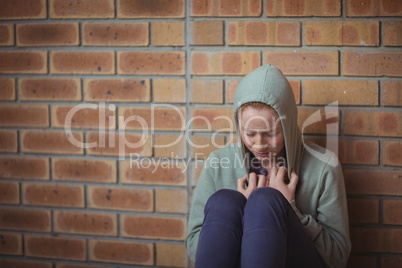 Sad schoolgirl sitting alone against brick wall