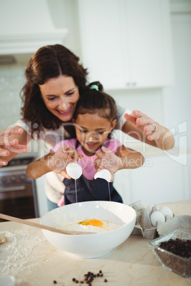 Mother and daughter breaking egg in bowl while preparing cookie