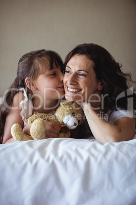 Daughter kissing her mother on cheek in bedroom