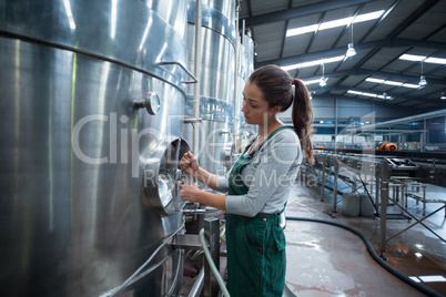 Female factory worker turning control wheel of storage tank