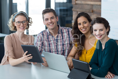 Smiling business executives sitting in office with digital tablet and laptop on table