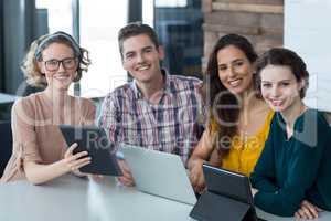Smiling business executives sitting in office with digital tablet and laptop on table