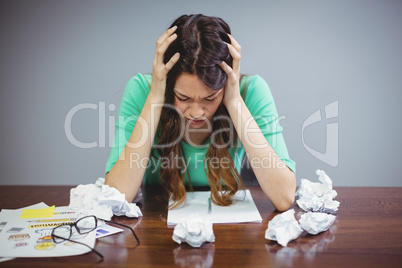Frustrated female executive sitting with crumpled papers balls