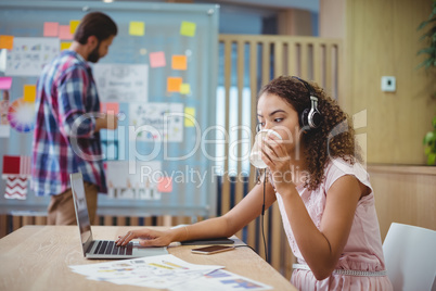 Female graphic designer drinking coffee while using laptop