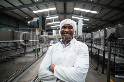 Smiling factory engineer standing with arms crossed in bottle factory