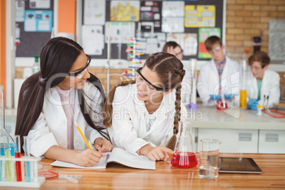 School girls writing in journal book while experimenting in laboratory at school