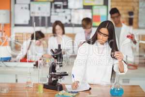School girl writing in journal book while experimenting in laboratory