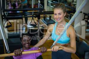 Smiling trainer assisting woman with pilates on reformer