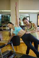 Female trainer assisting woman with stretching exercise on reformer