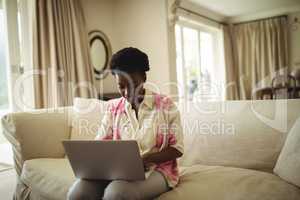 Woman sitting on sofa and using laptop in living room