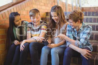 Smiling school students sitting on the staircase using mobile phone