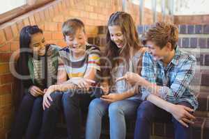 Smiling school students sitting on the staircase using mobile phone