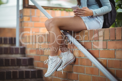 Schoolgirl sitting on brick wall and using mobile phone