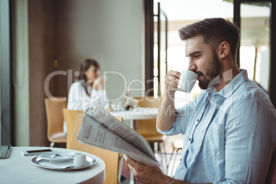 Executive reading newspaper while having coffee