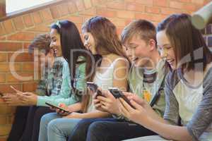 Group of smiling school friends sitting on staircase using mobile phone