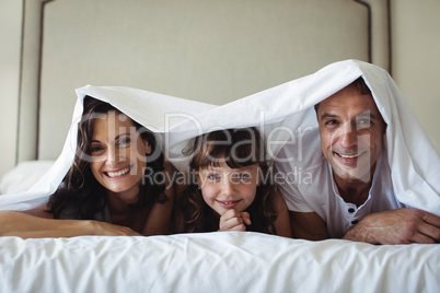 Happy family lying under blanket on bed at home