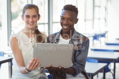 Schoolkids holding laptop in classroom